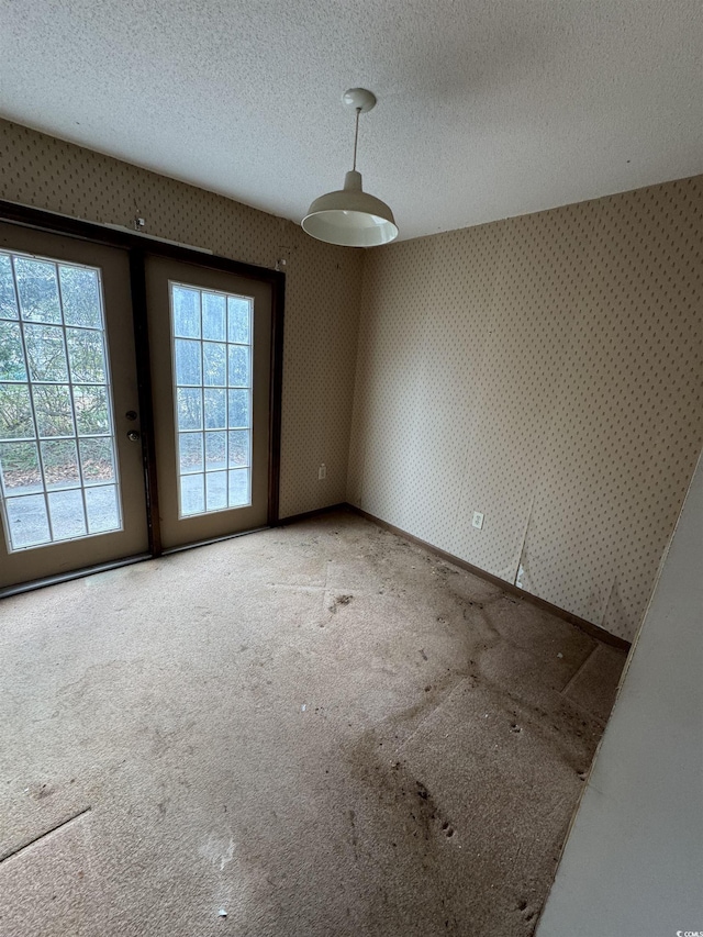 carpeted spare room with a textured ceiling, wallpapered walls, and baseboards