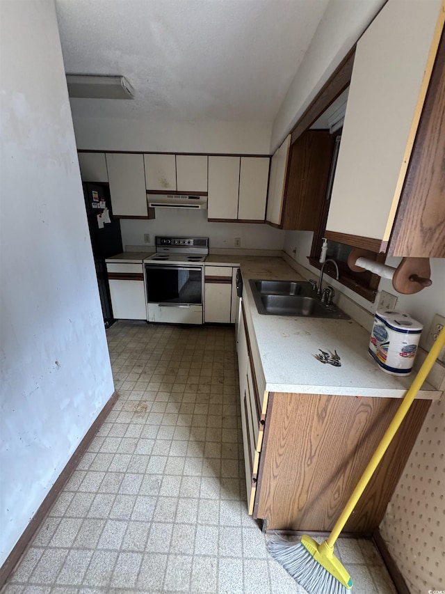 kitchen featuring a sink, range hood, freestanding refrigerator, white electric stove, and light countertops