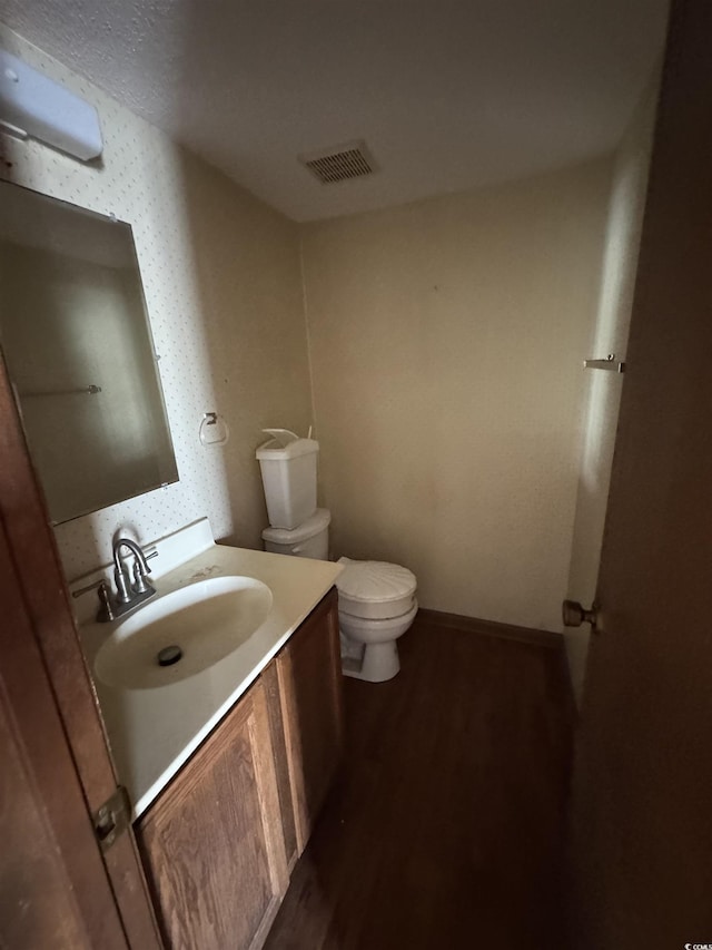 bathroom featuring vanity, wood finished floors, visible vents, baseboards, and toilet