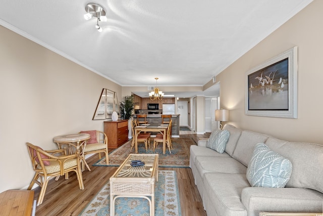 living room with light wood-type flooring, an inviting chandelier, and ornamental molding