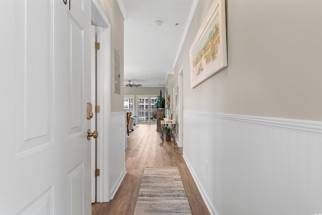 hall with a wainscoted wall, ornamental molding, and wood finished floors