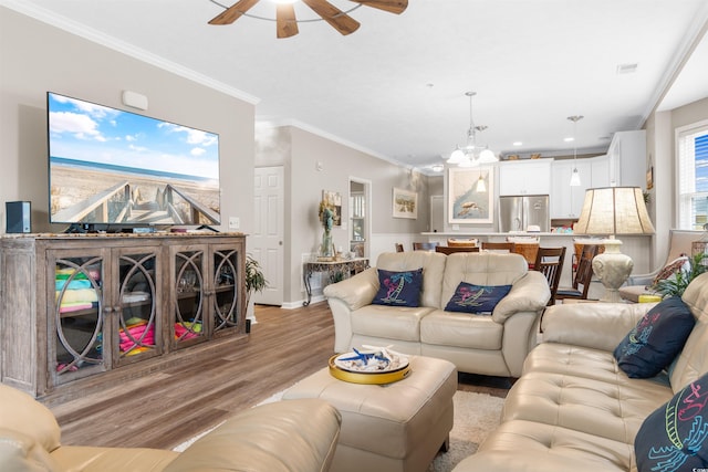 living room featuring visible vents, ceiling fan with notable chandelier, crown molding, and light wood-style floors