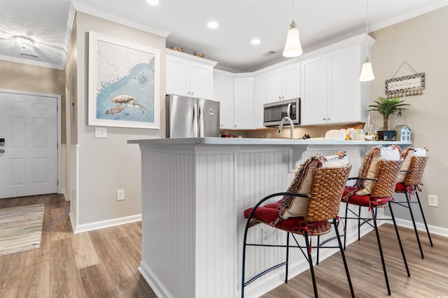 kitchen with white cabinets, stainless steel appliances, crown molding, and light wood-style floors