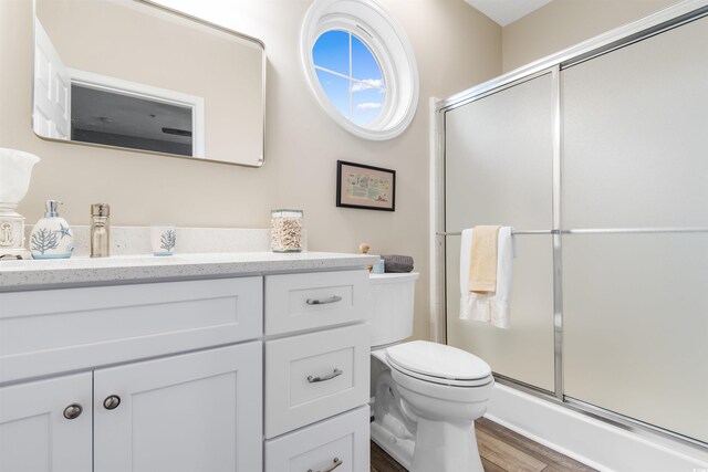 bathroom featuring vanity, toilet, wood finished floors, and a stall shower