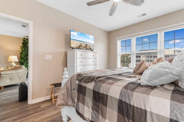 bedroom featuring visible vents, a textured ceiling, wood finished floors, baseboards, and ceiling fan