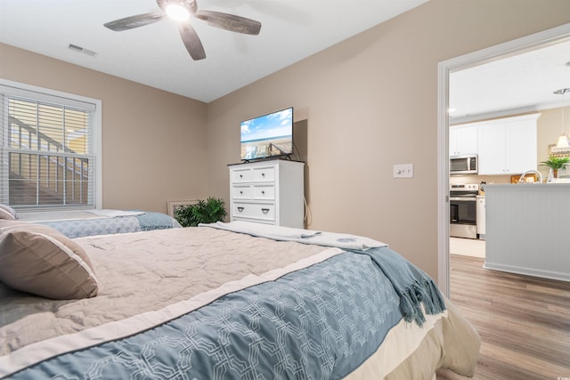 bedroom with a sink, light wood-type flooring, visible vents, and a ceiling fan