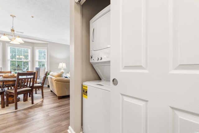 washroom featuring light wood-type flooring, an inviting chandelier, laundry area, and stacked washing maching and dryer