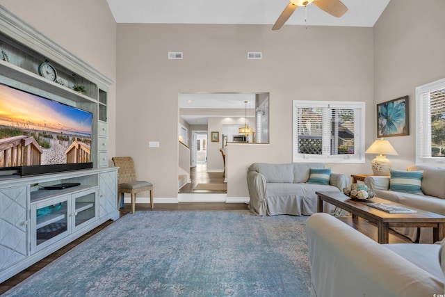 living area with visible vents, a ceiling fan, a towering ceiling, and wood finished floors