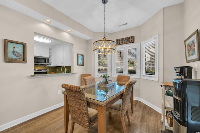 dining space with baseboards, visible vents, wood finished floors, and a notable chandelier