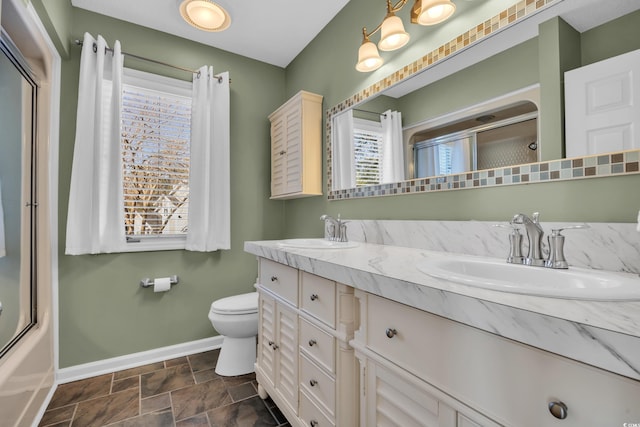 full bath featuring baseboards, a sink, double vanity, and toilet