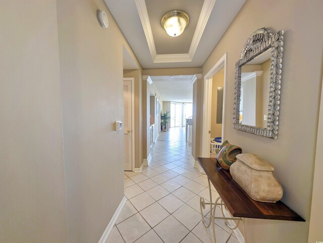 corridor featuring a tray ceiling, baseboards, light tile patterned flooring, and ornamental molding