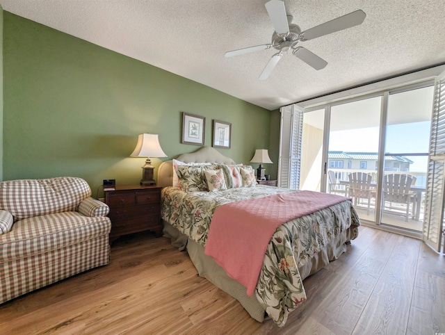 bedroom with floor to ceiling windows, a textured ceiling, wood finished floors, and access to outside