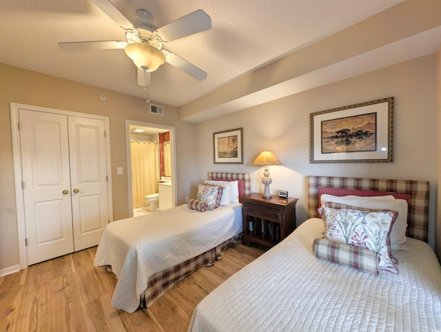 bedroom featuring light wood finished floors, visible vents, ensuite bathroom, a closet, and a ceiling fan