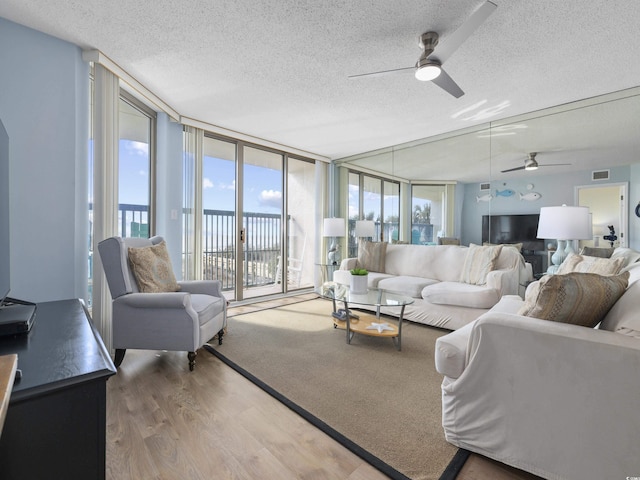 living room featuring visible vents, a ceiling fan, a textured ceiling, wood finished floors, and a wall of windows