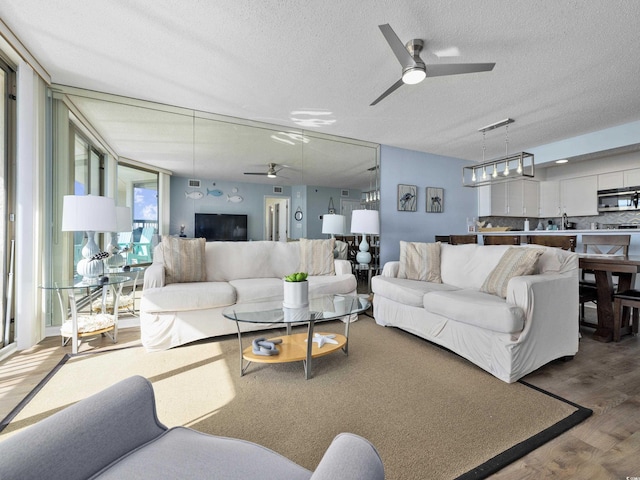 living room featuring a ceiling fan, floor to ceiling windows, wood finished floors, and a textured ceiling