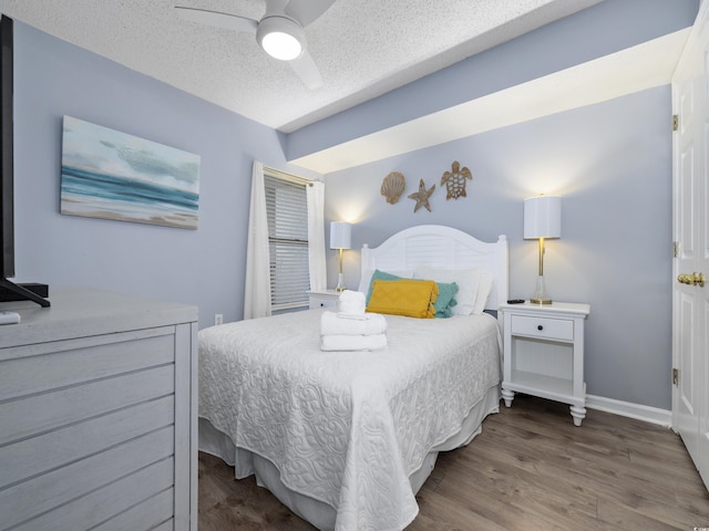 bedroom with ceiling fan, wood finished floors, baseboards, and a textured ceiling