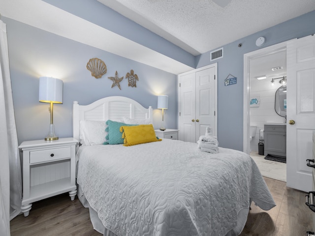 bedroom featuring wood finished floors, visible vents, a closet, a textured ceiling, and connected bathroom
