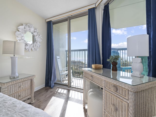 bedroom with access to outside, wood finished floors, baseboards, and a textured ceiling