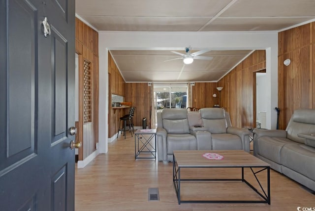 living room with wooden walls, light wood-style flooring, a ceiling fan, and visible vents