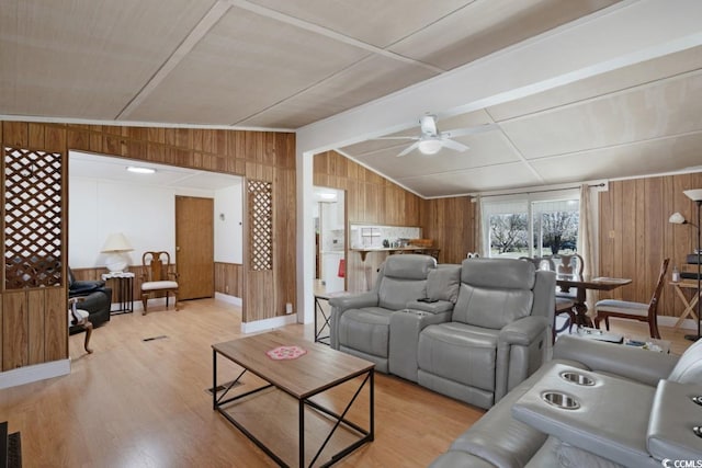 living room with a ceiling fan, wooden walls, vaulted ceiling with beams, and light wood-style flooring