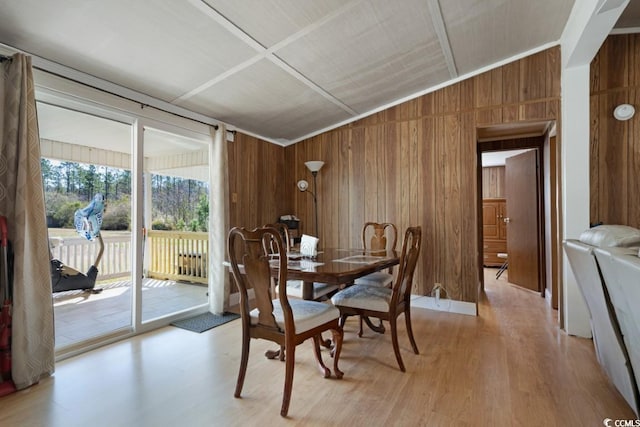 dining space with wooden walls, light wood-style flooring, and vaulted ceiling