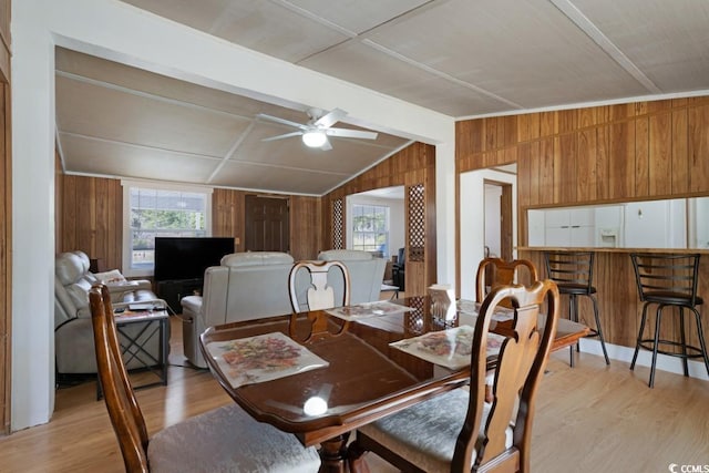 dining area with wooden walls, a ceiling fan, lofted ceiling with beams, and light wood-style floors