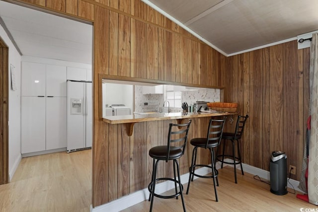 kitchen with washer and dryer, white refrigerator with ice dispenser, brown cabinetry, and light wood finished floors