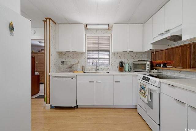 kitchen with white appliances, a sink, light countertops, under cabinet range hood, and light wood-type flooring