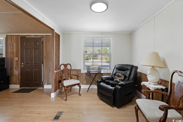 living area featuring wooden walls, visible vents, crown molding, a wainscoted wall, and light wood-style floors