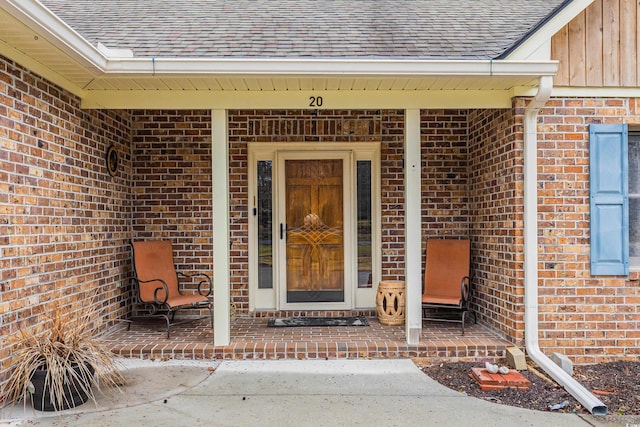 doorway to property featuring brick siding and roof with shingles