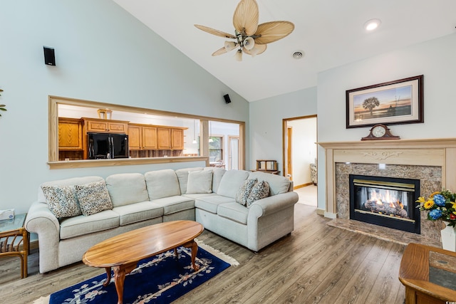 living area featuring visible vents, light wood finished floors, high vaulted ceiling, a high end fireplace, and ceiling fan