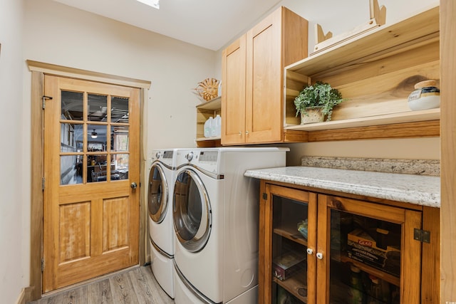 laundry room with washing machine and clothes dryer, cabinet space, and light wood-style floors