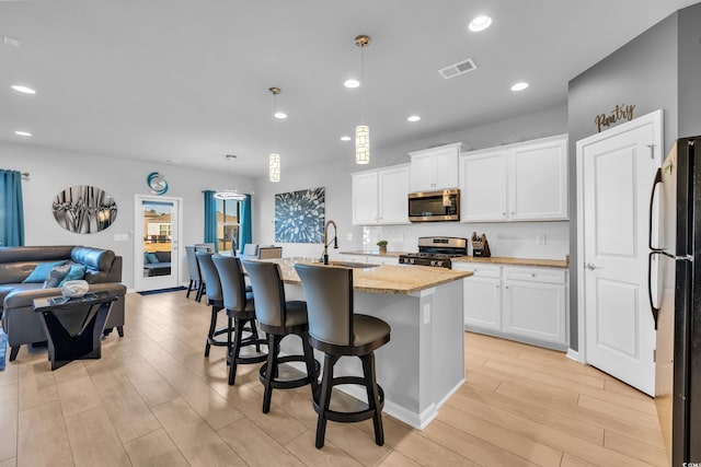 kitchen featuring visible vents, a sink, open floor plan, appliances with stainless steel finishes, and light stone countertops