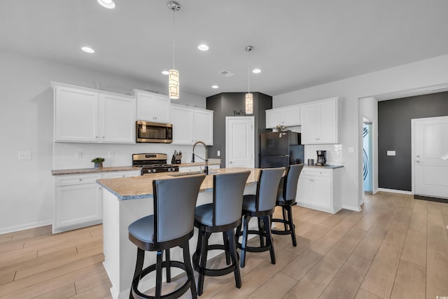 kitchen with a sink, a kitchen breakfast bar, stainless steel appliances, light wood-style floors, and decorative backsplash