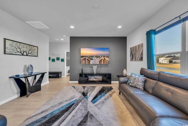 living area featuring light wood finished floors, visible vents, recessed lighting, and a glass covered fireplace