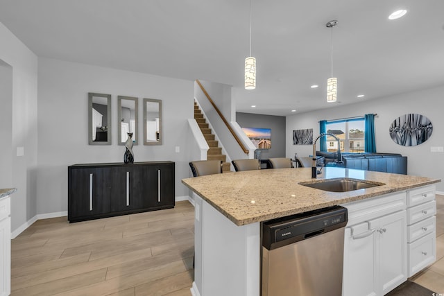 kitchen featuring light stone countertops, a sink, hanging light fixtures, light wood-style floors, and dishwasher