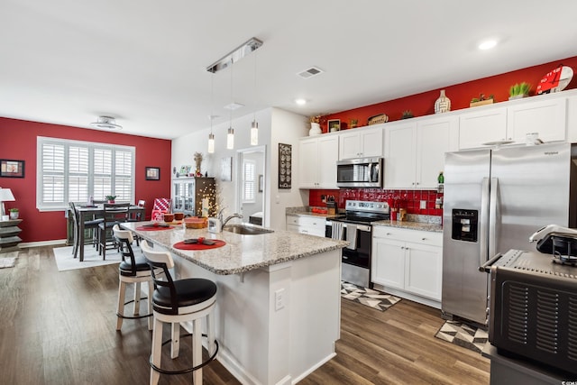 kitchen featuring visible vents, dark wood-type flooring, appliances with stainless steel finishes, a kitchen breakfast bar, and backsplash