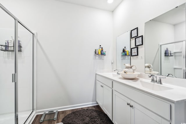 bathroom with a shower stall, wood finished floors, double vanity, and a sink