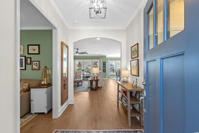 entrance foyer with ceiling fan with notable chandelier, wood finished floors, arched walkways, and ornamental molding