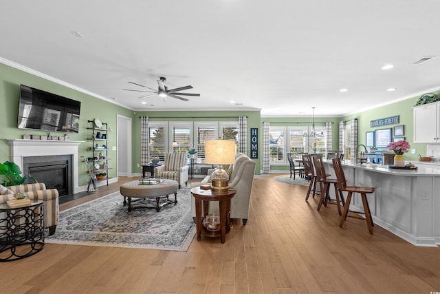 living room with a fireplace with flush hearth, light wood-style flooring, crown molding, and visible vents