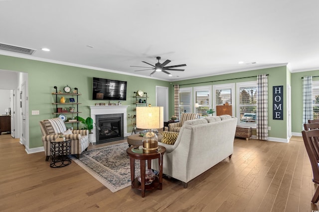 living room with a fireplace with flush hearth, wood finished floors, visible vents, and ornamental molding