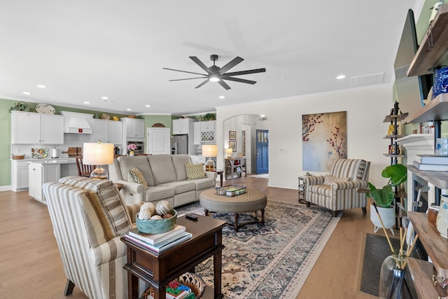 living room with recessed lighting, arched walkways, light wood-style floors, and crown molding