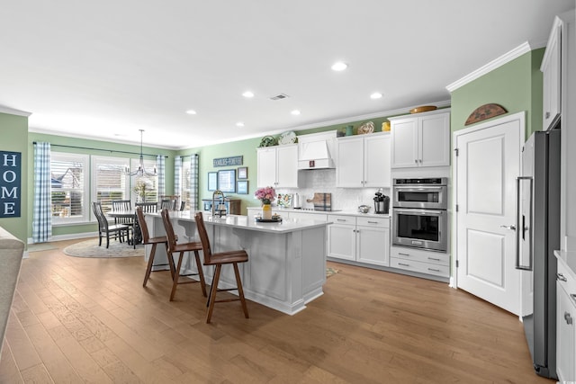 kitchen featuring visible vents, light wood finished floors, a kitchen island with sink, decorative backsplash, and appliances with stainless steel finishes