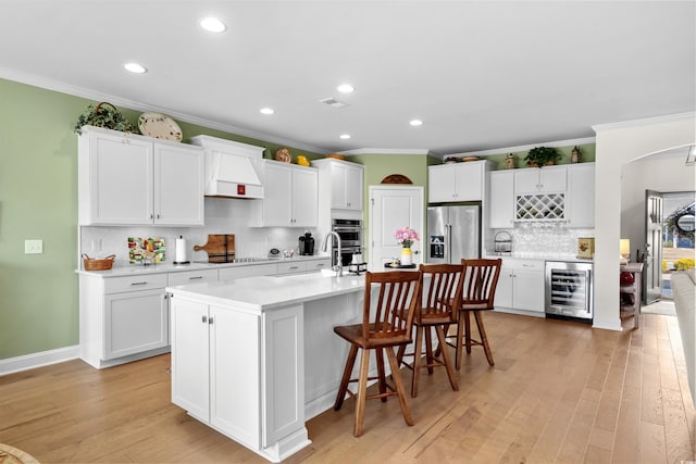 kitchen featuring wine cooler, light countertops, light wood-style flooring, appliances with stainless steel finishes, and white cabinetry