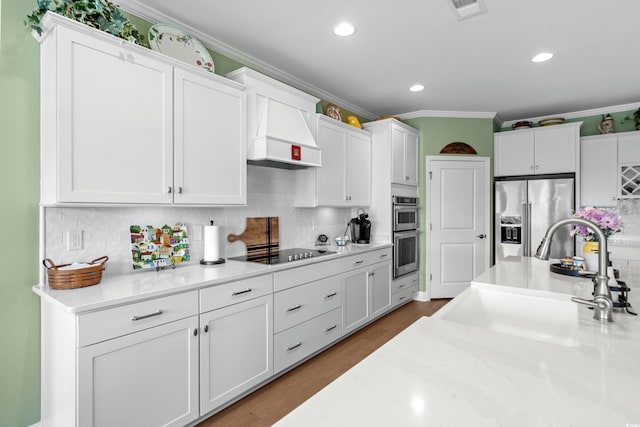 kitchen featuring crown molding, custom range hood, appliances with stainless steel finishes, white cabinetry, and a sink