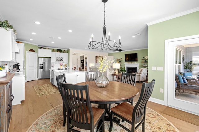 dining space featuring light wood finished floors, ornamental molding, recessed lighting, a warm lit fireplace, and arched walkways