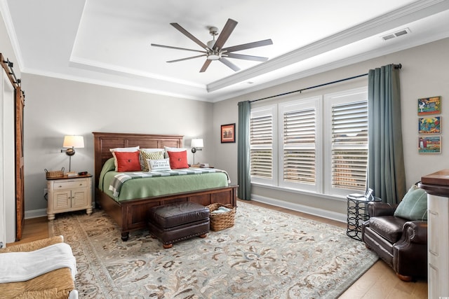 bedroom featuring a barn door, crown molding, visible vents, and a raised ceiling