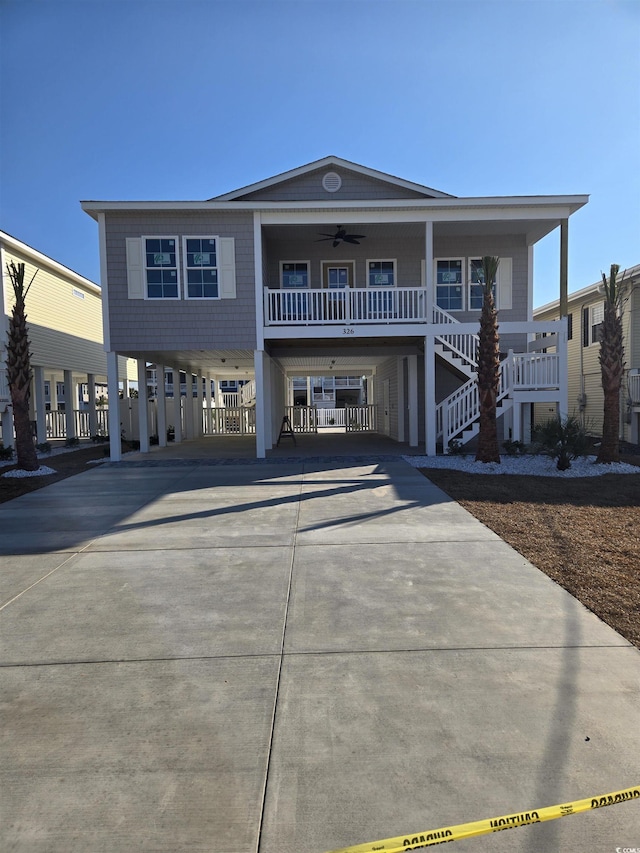 raised beach house with a carport, stairway, covered porch, and concrete driveway