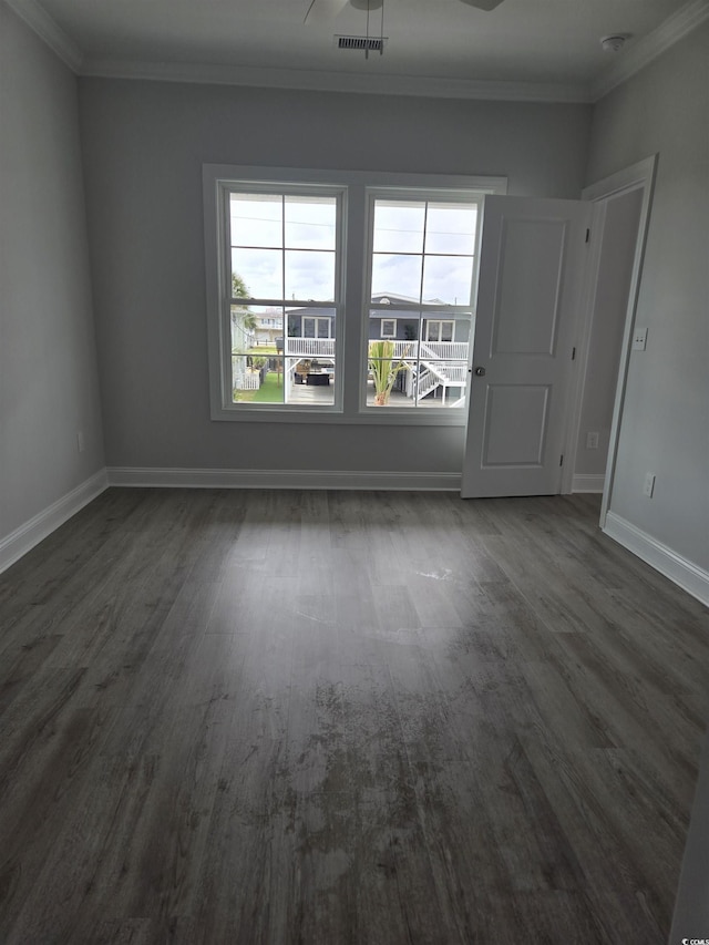 empty room featuring visible vents, baseboards, dark wood-style floors, and ornamental molding