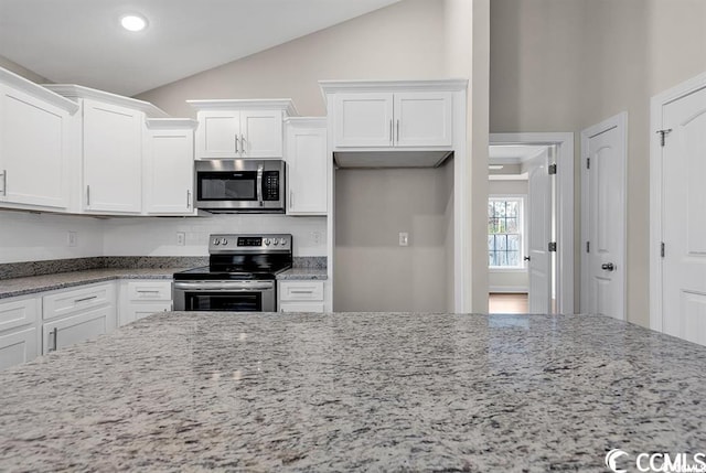 kitchen featuring white cabinets, appliances with stainless steel finishes, lofted ceiling, and light stone countertops